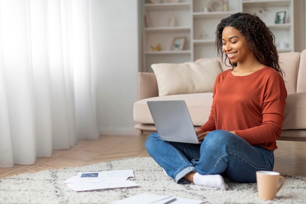 Zwarte vrouw die thuis op de vloer zit met een laptop.