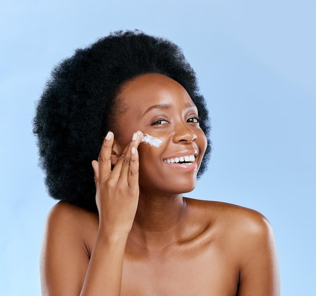 Zwarte vrouw gezicht en crème schoonheid en cosmetische zorg met glimlach en huidverzorging op blauwe achtergrond Moisturizer lotion en product voor de huid met zonnebrandcrème en portret vrouwelijk model en dermatologie