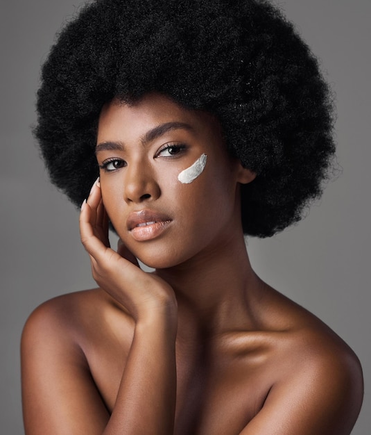 Zwarte vrouw in portretcrème en schoonheid met huidverzorgings- en cosmeticaproduct op studioachtergrond Natuurlijk afrokapsel en Afrikaans vrouwelijk model dermatologie met lotion en gezichtsbevochtiger