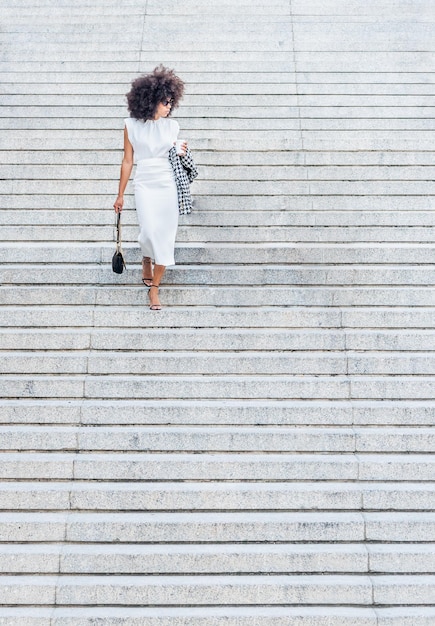 Zwarte vrouw loopt alleen de trap af en kijkt opzij in een witte jurk
