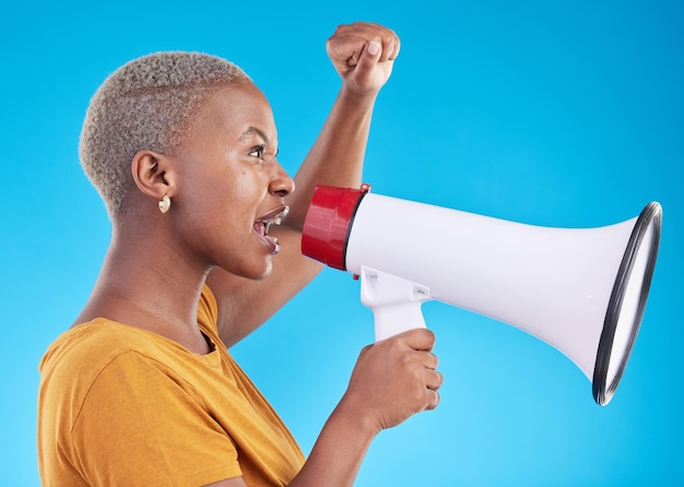 Foto zwarte vrouw megafoon en protest in studio schreeuwen of profiel met vuist in de lucht voor mensenrechten door blauwe achtergrond afrikaans gen z studentenmeisje en audiotechnologie voor machtsopinie of nieuwsaankondiging