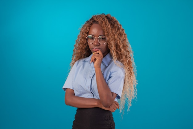 Zwarte vrouw met krullend haar in studiofoto die blauw overhemd en zwarte rok draagt en diverse gezichtsuitdrukkingen maakt.