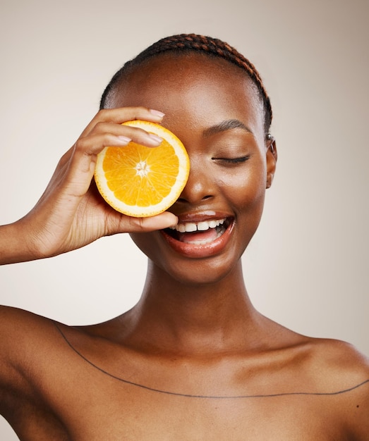 Zwarte vrouw oranje fruit en huidverzorging in studio voor vitamine C veganistische dermatologie en cosmetica op bruine achtergrond Gelukkig model citrusdieet en voeding voor natuurlijke schoonheid organische gezichts- of glans