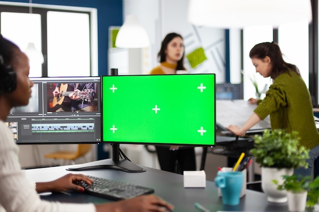 Zwarte vrouw videograaf werknemer met koptelefoon met behulp van computer met groen scherm, chroma key mockup geïsoleerd display zittend in videoproductie studio