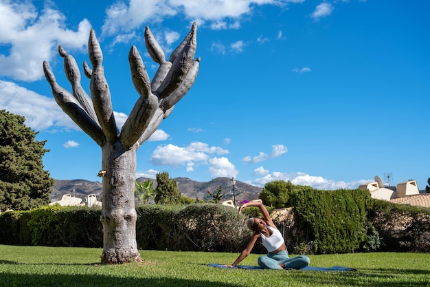 Zwarte vrouw zittend op mat op met gras begroeid gazon in de tuin en het beoefenen van yoga en stretching