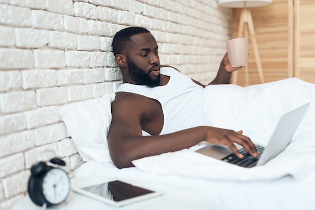 Zwarte wakende man drinkt koffie in bed