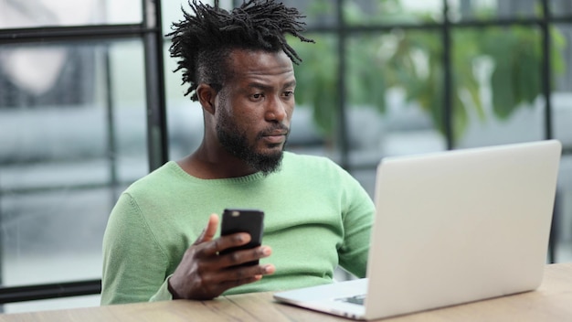 Zwarte zakenman die op een mobiele telefoon op kantoor praat terwijl hij een laptop gebruikt