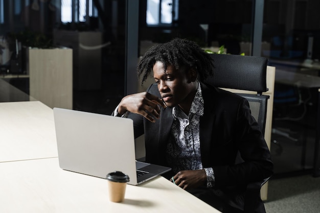 Zwarte zakenman met laptop werkt online op kantoor. Knappe afrikaanse manager doet werk op afstand in coworking-ruimte.