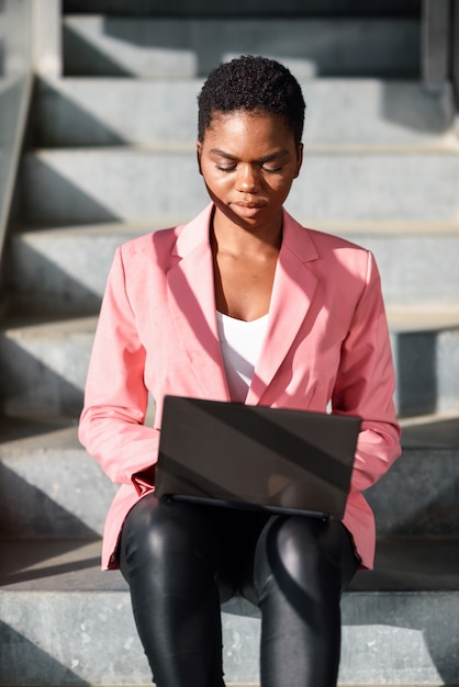 Zwartezitting op stedelijke stappen die met een laptop computer werken