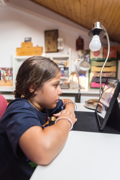 Foto zwartharig meisje met een blauw t-shirt kijkend naar een tablet in een huiskamer jeugd technologie onderwijs verslaving tablet internetverbinding en relax concept