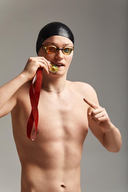 Zwemmer met een medaille op een grijze achtergrond verheugt zich in de overwinning een atleet in uitstekende fysieke vorm viert een overwinning met een medaille in zijn hand geklemd overwinningsconcept grijze achtergrond kopie ruimte