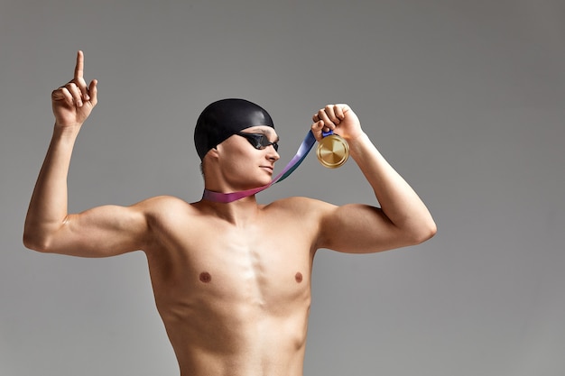 Zwemmer met een medaille op een grijze achtergrond verheugt zich in de overwinning, een atleet in uitstekende fysieke vorm viert een overwinning met een medaille in zijn hand, overwinningsconcept, grijze achtergrond, kopieerruimte.