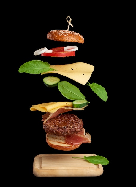 Zwevende ingrediënten van cheeseburger: sappige vleeskotelet, cheddarkaas, sesambroodje, sla, witte uienringen, plakje tomaat, komkommer