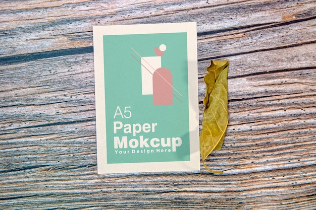 木製の背景に乾燥した葉と a5 用紙グリーティング カード モックアップ