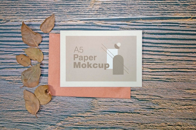 A5 paper greeting card mockup with dry leaves on wooden background