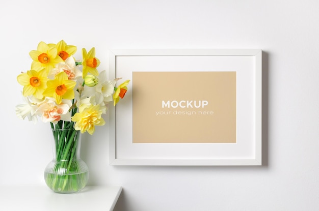 Artwork frame mockup with spring daffodils flowers in white room interior