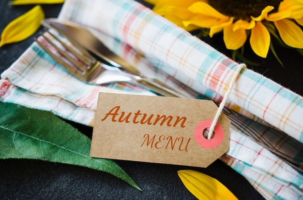 Autumn table place setting with empty tag, cutlery with napkin and sunflower.