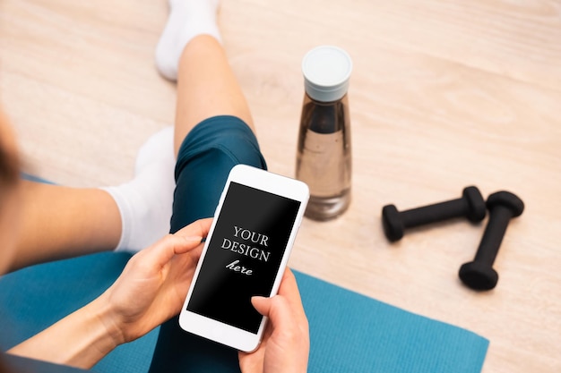 PSD back view of sportive woman resting on the floor using modern smartphone mockup