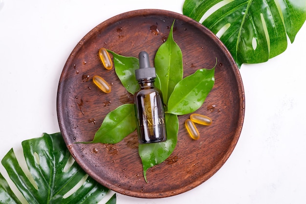 Beauty natural products with Omega-3 gel capsules and serum in glass bottles , green leaves on wooden plate on white background.