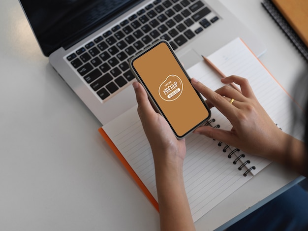 Bijgesneden schot van zakenvrouw met mock-up smartphone in haar werkruimte