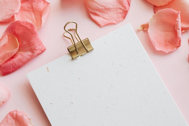 Blank binder clip paper mockup with light pink background and pink rose petals