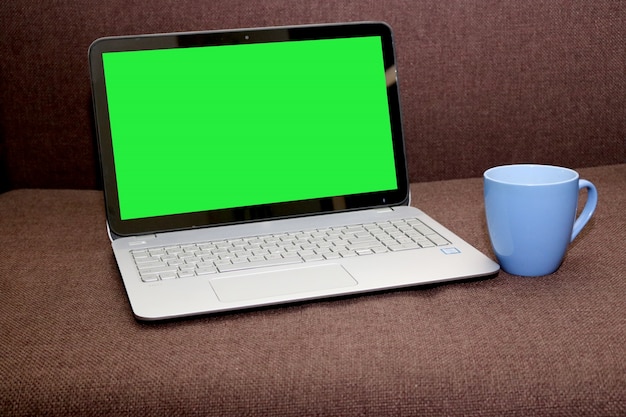 Blank green screen laptop with tea cup
