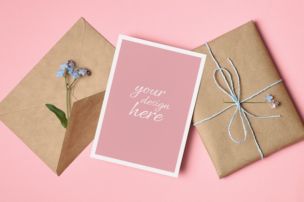 Mockup di biglietto di auguri in bianco con busta regalo e fiori