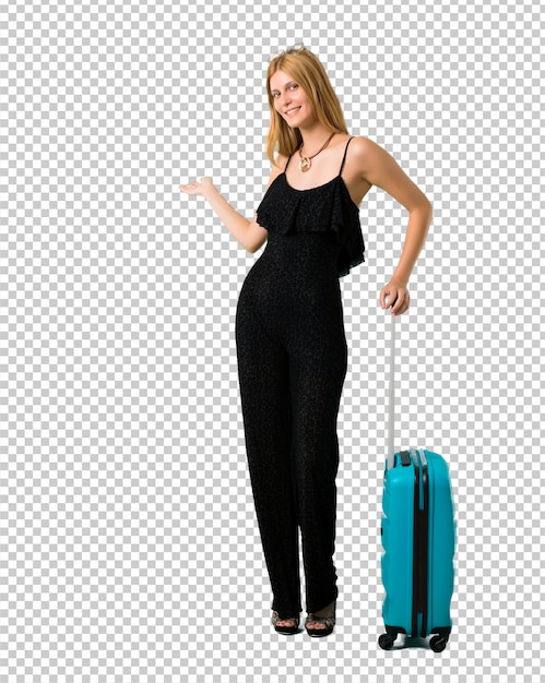 Blond girl traveling with her suitcase pointing back with the index finger presenting a product