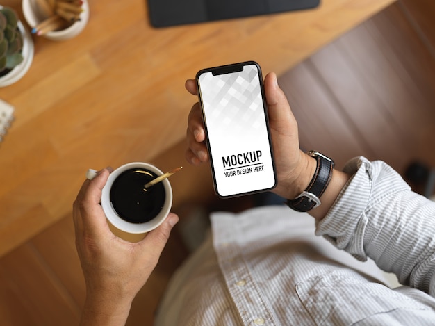 Bovenaanzicht van mannenhand met smartphone mockup en koffiekopje