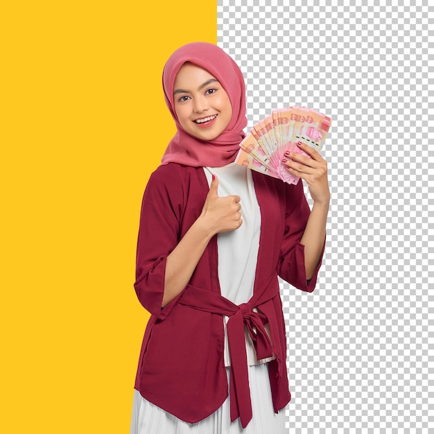 Cheerful beautiful asian woman in casual shirt holding indonesian rupiah banknotes and showing thumb up gesture