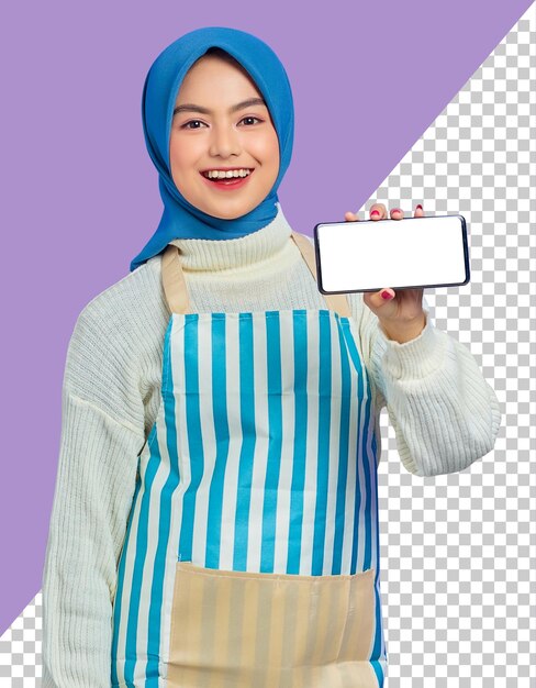 Cheerful young asian muslim woman wearing hijab and apron holding blank screen mobile phone with hand isolated on purple background people housewife muslim lifestyle concept