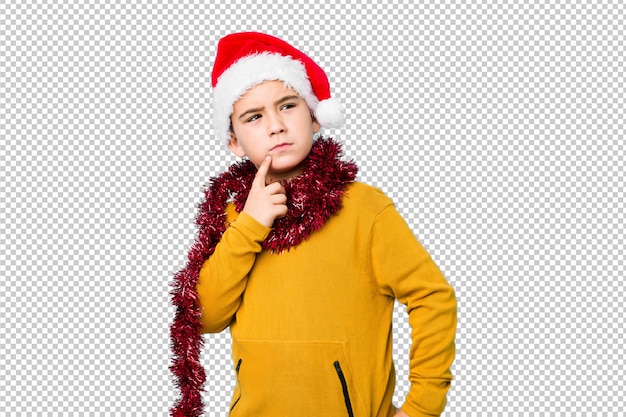 Chłopiec świętuje boże narodzenie dzień jest ubranym Santa kapelusz odizolowywał patrzeć z ukosa z wątpliwym i sceptycznym wyrażeniem.
