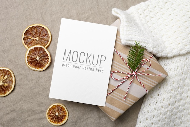 Christmas greeting card mockup with decorated gift box, knitted sweater and dry oranges