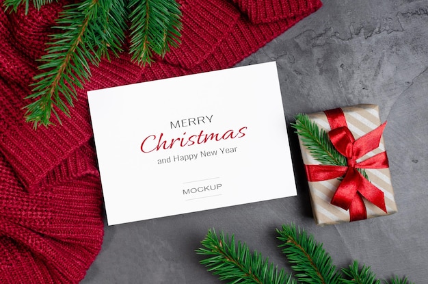Modello di biglietto di auguri di natale con scatola regalo e rami di abete su sfondo rosso a maglia Psd Premium