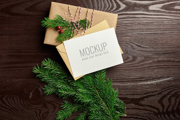 Christmas greeting card mockup with gift box and fir tree branches on wooden background