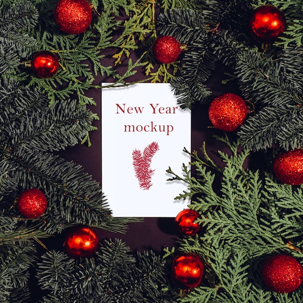 Christmas mockup, white sheet of paper lying on spruce branches, red Christmas balls.