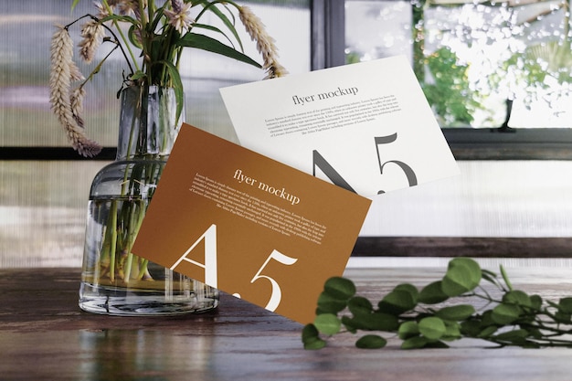 Clean minimal a5 flyer mockup floating on wooden table with vase and plant psd file