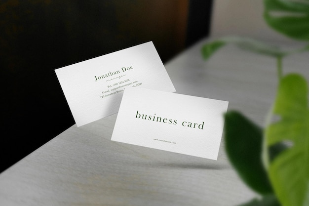 Clean minimal business card mockup floating on desktop with leaves background. PSD file.