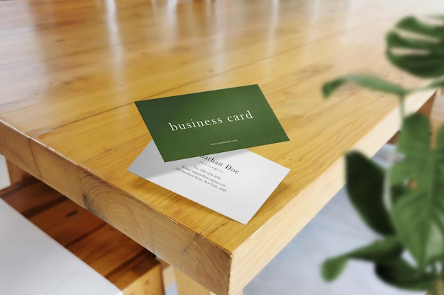 clean minimal business card mockup floating on top table with leaves background. psd file.