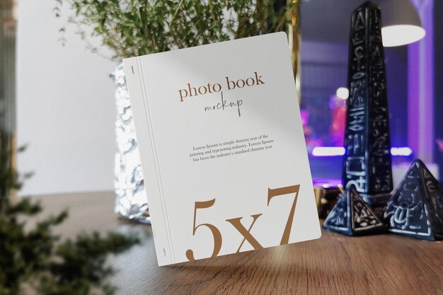 Clean minimal photo book 5x7 mockup standing on wooden top with plant background psd file