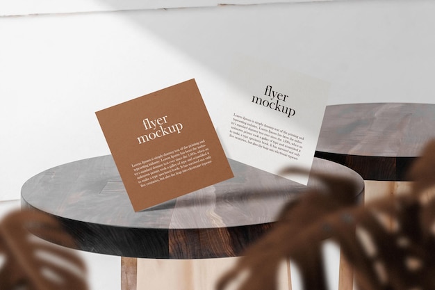 Clean minimal square flyer mockup floating on top table with leaves.