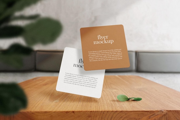 Clean minimal square flyer mockup floating on wooden table with plant and leaves