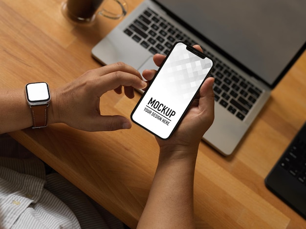 ホームオフィスルームでラップトップとワークテーブルでスマートフォンを使用してビジネスマンのクローズアップ