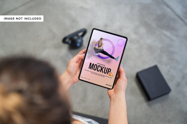 ジムの背景にタブレットのモックアップを持っている手を閉じる