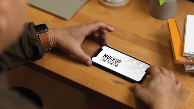 Close up of male hands using mockup smartphone on wooden table