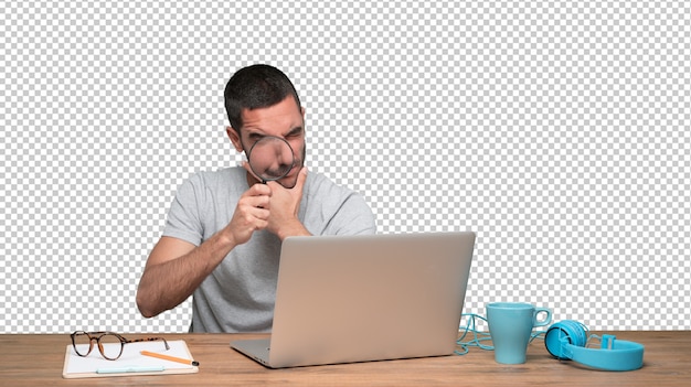 Concentrated young man using a magnifying glass on his laptop