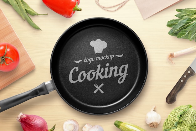 Cooking, restaurant logo mockup. pan on the kitchen table surrounded by vegetables. top view, flat lay