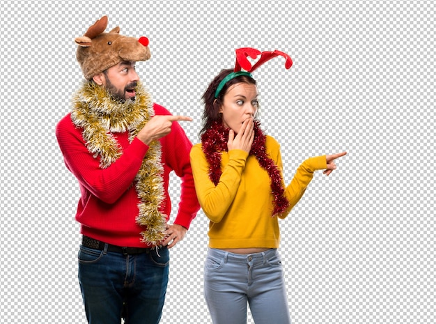 PSD couple dressed up for the christmas holidays pointing finger to the side with a surprised face