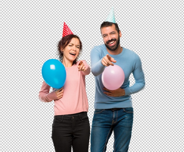 Пара с воздушными шарами и день рождения шляпы, указывая пальцем на кого-то и много смеется