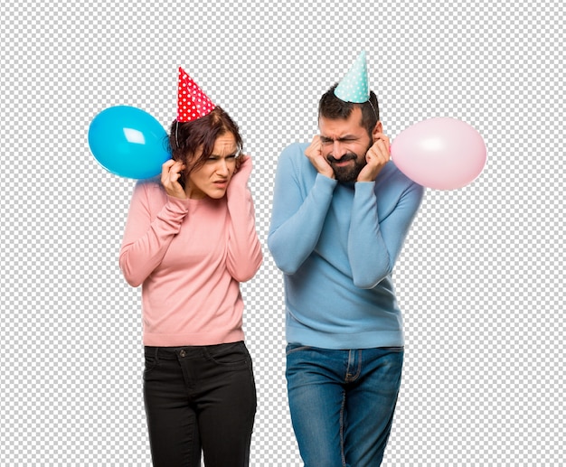 Couple with balloons and birthday hats covering ears with hands. frustrated expression